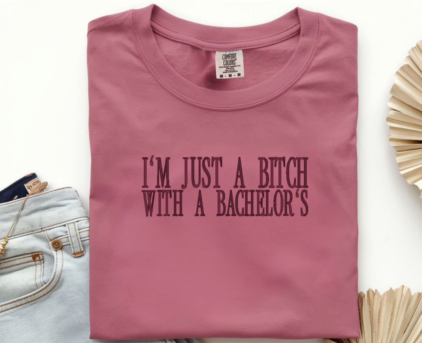Pink t-shirt with text 'I'm just a bitch with a bachelor's' on a white background