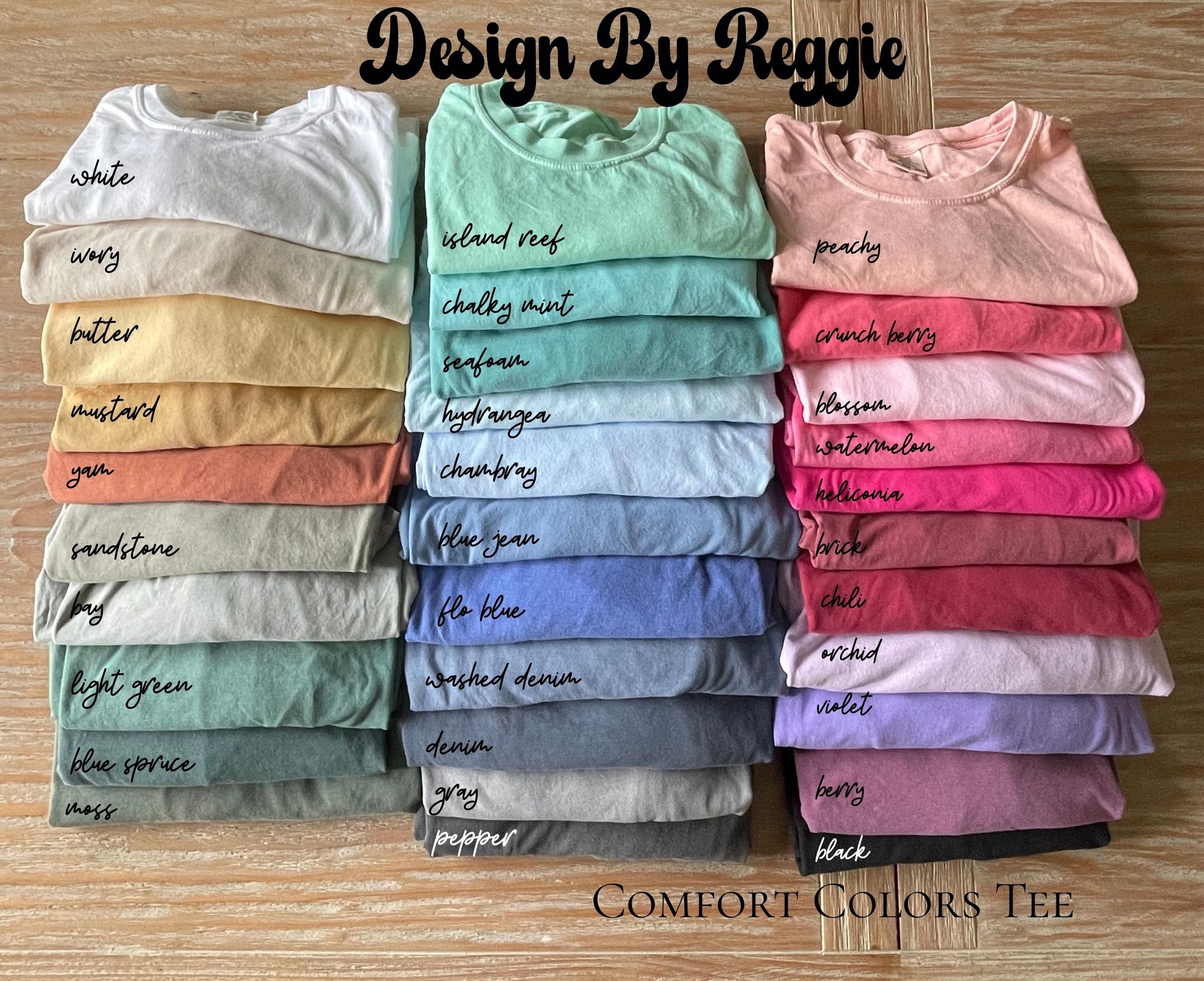 Stack of colorful t-shirts with color names on a wooden surface, labeled 'Design By Reggie'.